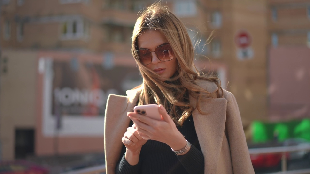 被吸收的高加索千禧一代女性站在阳光明媚的城市里用智能手机在线聊天。集中年轻苗条美丽女士的肖像冲浪社交媒体户外。视频素材