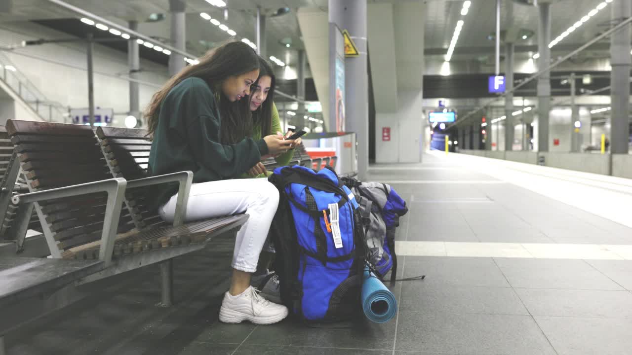 兩名年輕的女乘客在車站等火車時使用智能手機視頻素材
