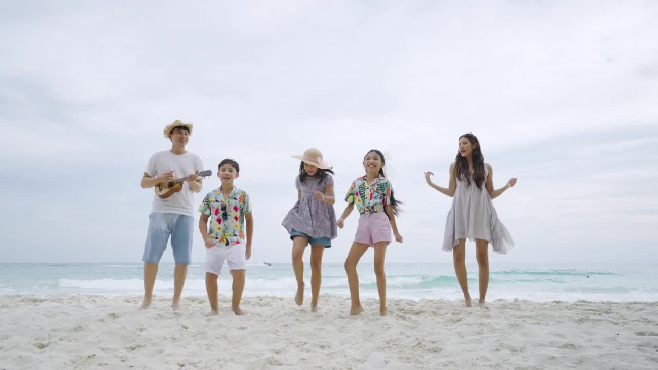 一个亚洲家庭带着孩子在海滩上跳舞弹吉他视频下载