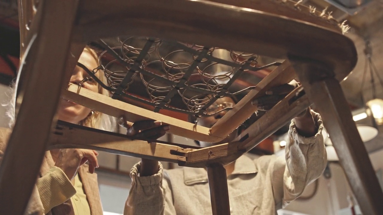 年轻的木匠在古董店为顾客调整古董椅上的弹簧视频下载