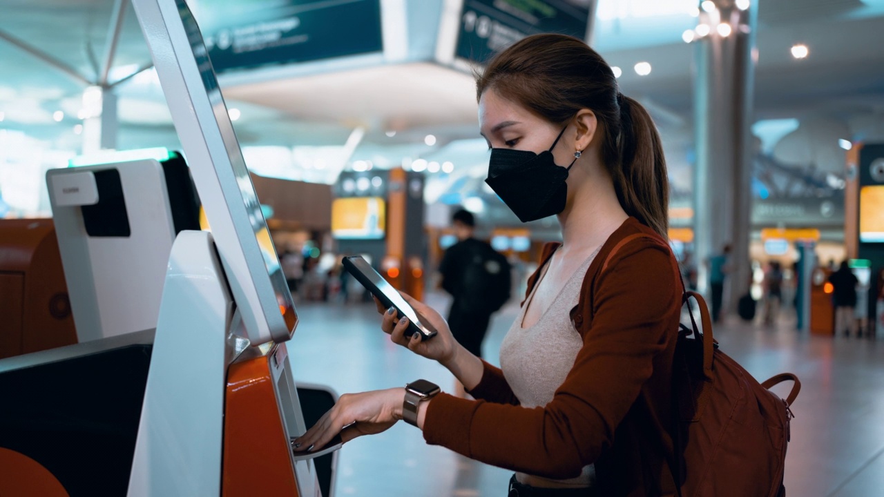 戴口罩的亚洲女性在机场自助值机柜台办理登机手续视频下载