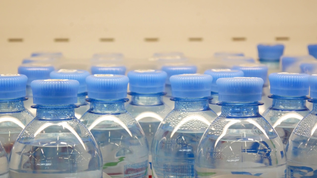 超市冰箱货架上许多漂亮的瓶装水的特写，一个男性买家的手拿着一瓶水视频素材