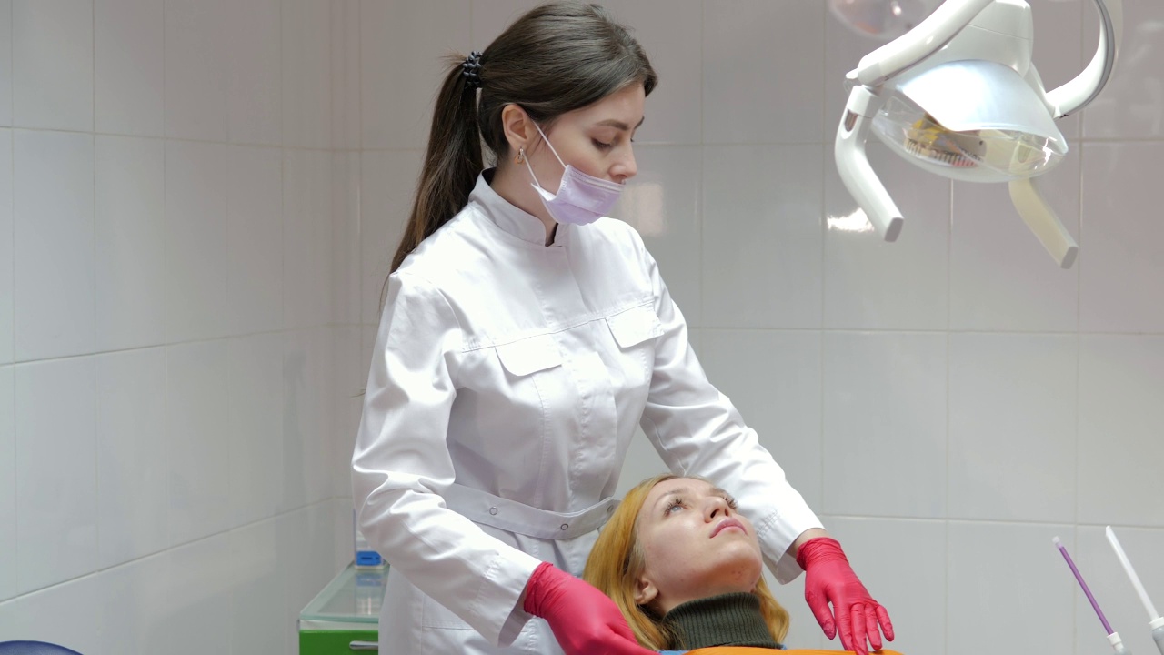 一个戴着面具的牙医在牙医预约时检查一个迷人的女孩的牙齿。戴着手套的牙医在病人的口腔内操作牙科器械。牙科诊所。牙科治疗。视频素材