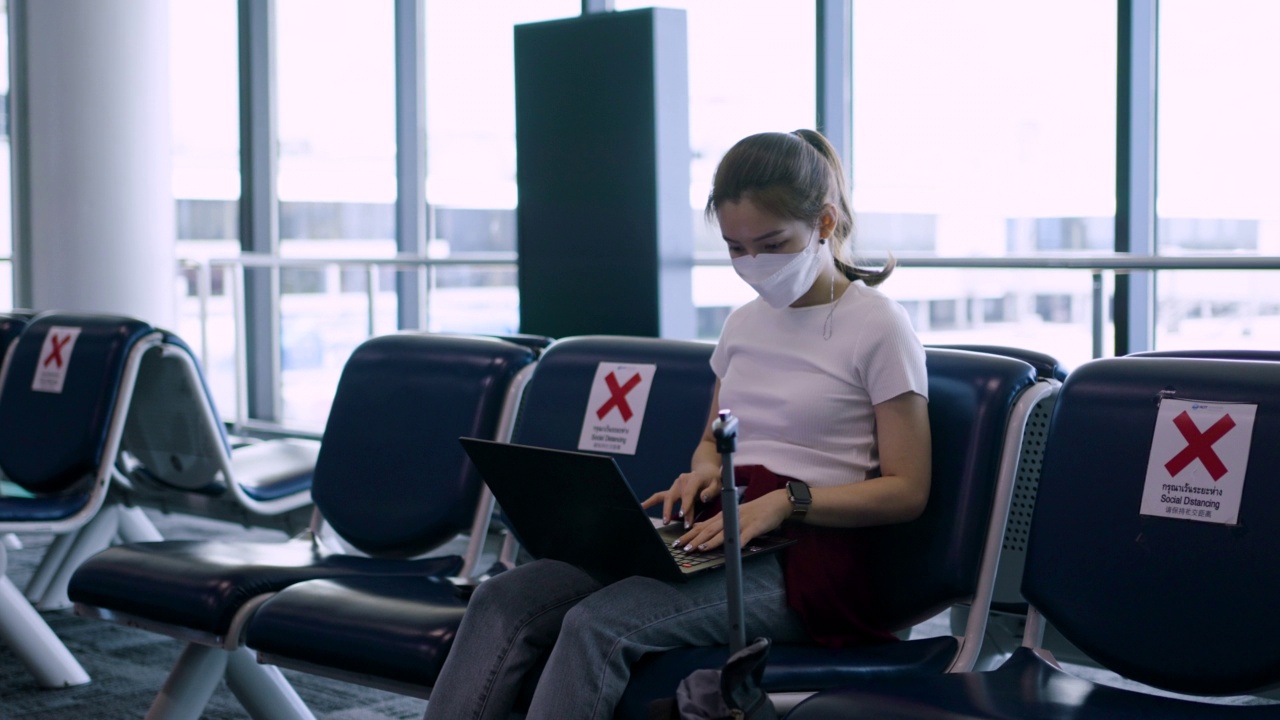 一名亚洲女性在候机候机时使用笔记本电脑在机场候机大厅工作视频下载