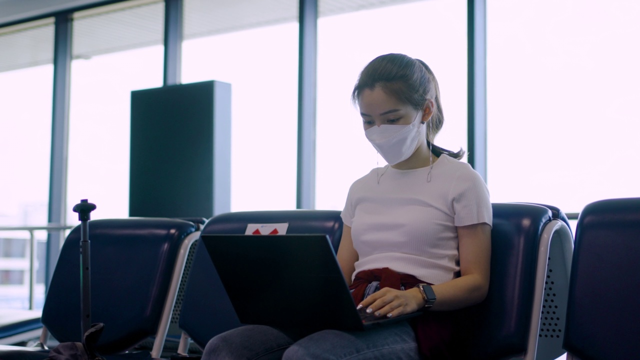 一名亚洲女性在候机候机时使用笔记本电脑在机场候机大厅工作视频下载