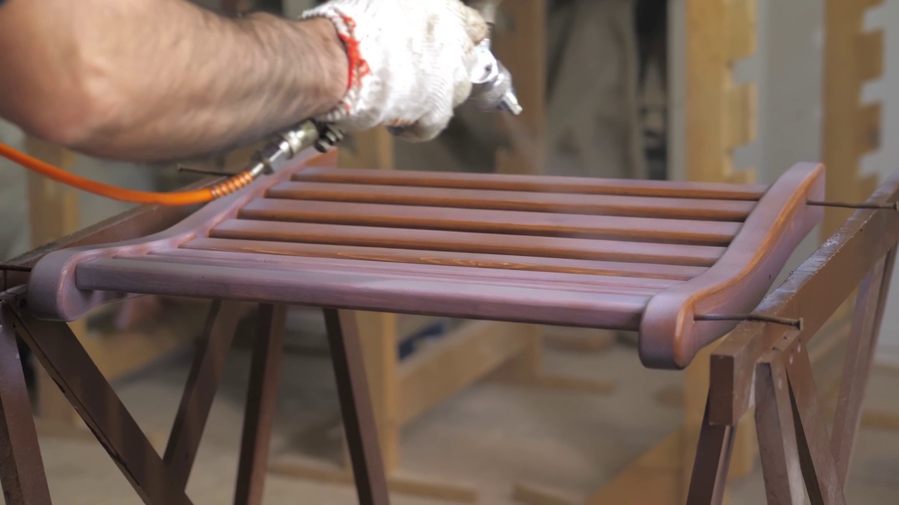 木匠们戴着手套，用压缩空气在木头表面涂上清漆或底漆。在木工车间用喷枪喷涂木制品。油漆和清漆涂层。特写。4 k视频素材