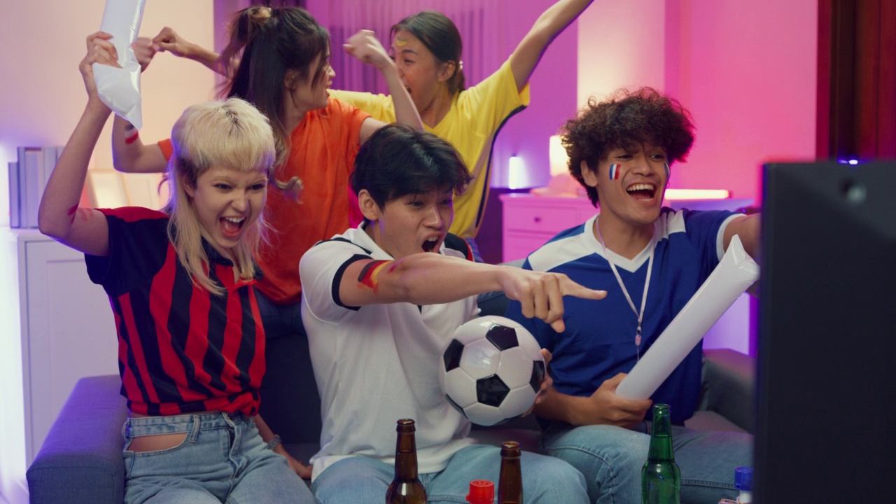 一群快乐的亚洲青少年晚上坐在沙发上看电视上的体育比赛。视频素材