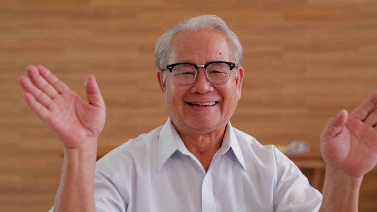 特写面部肖像的健康快乐的亚洲资深老人，白发老人微笑着向相机挥手，而在客厅。视频素材