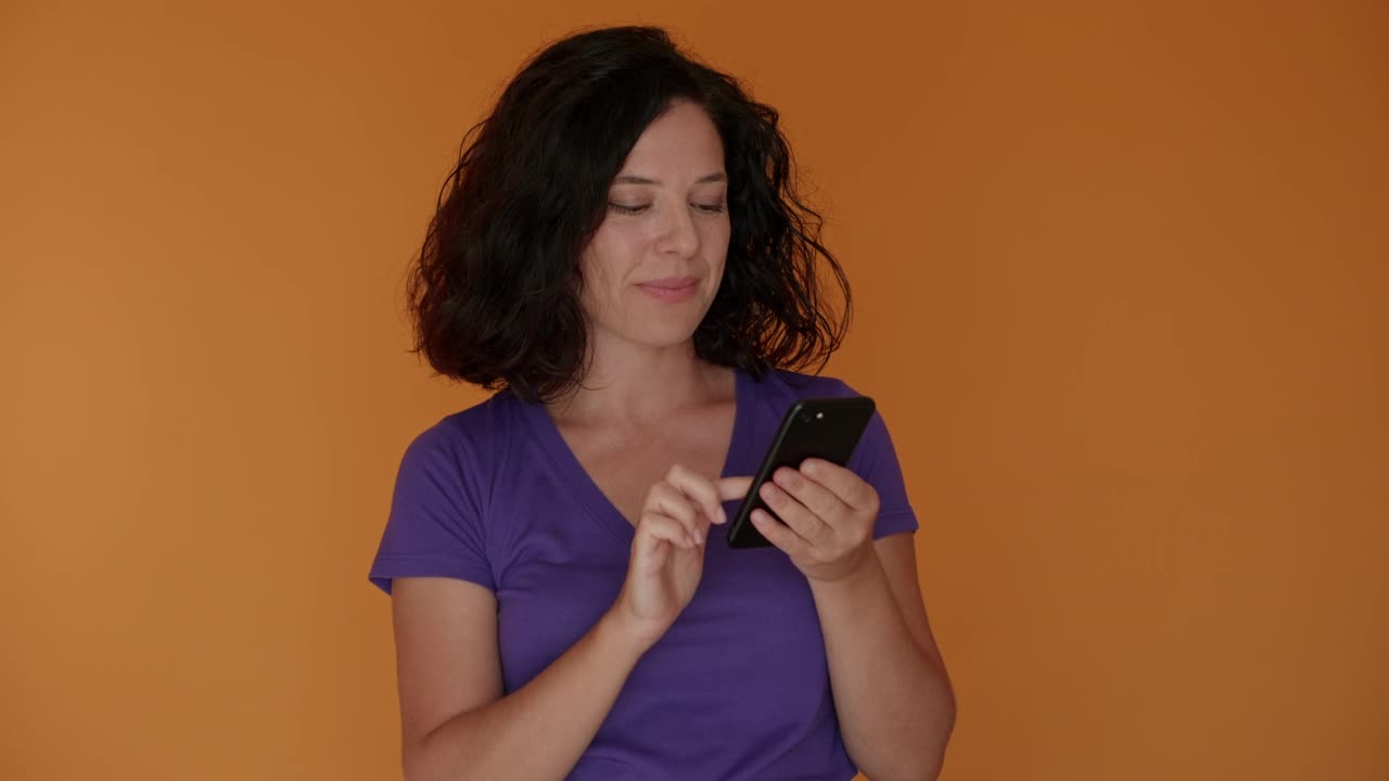 年轻女子打哈欠时，看着她的短信在她的手机在橙色的背景。视频素材