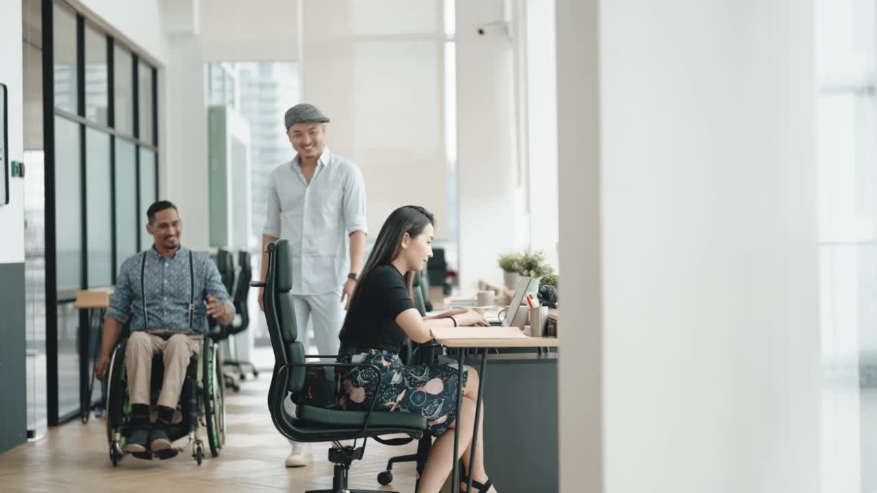 多元化亚裔印度白领坐在轮椅上与同事一起工作在创造性的办公室工作站视频素材