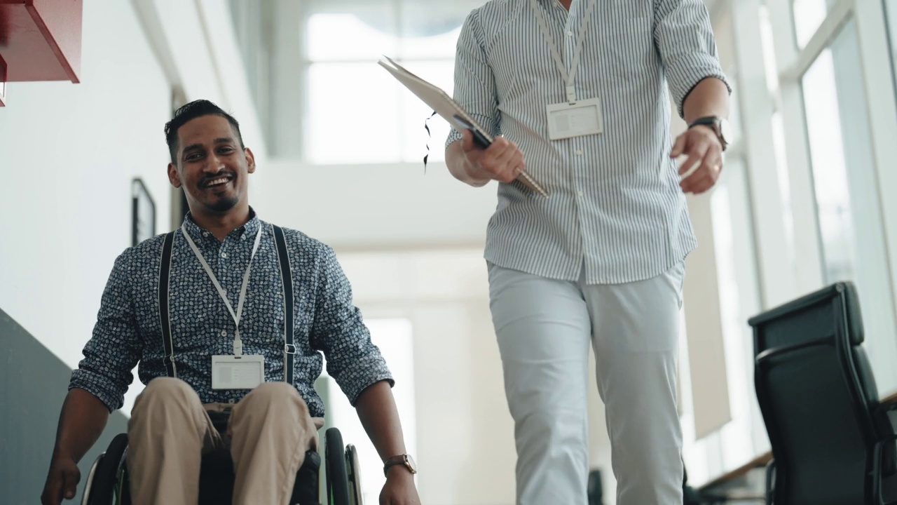 轮椅上的印度男性残疾白领与在走道走廊合作的亚裔中国男性同事讨论视频素材