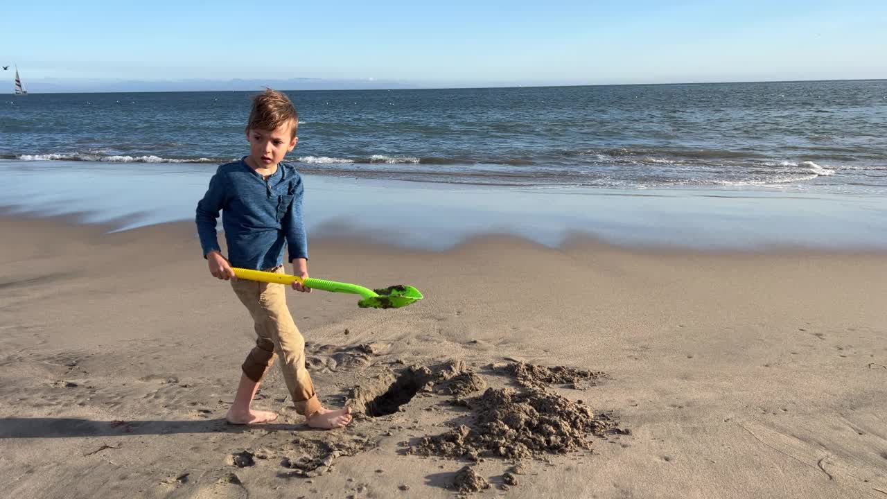 小男孩在沙滩上用铲子在沙地上挖洞视频下载