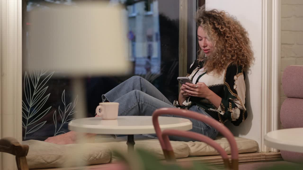 可爱的卷发女孩在咖啡馆用手机视频素材