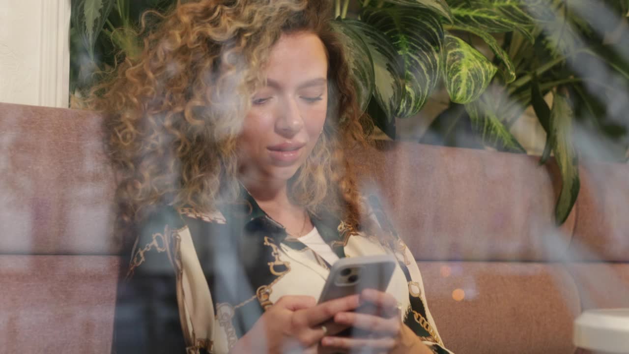 可爱的卷发女孩坐在咖啡馆靠窗和使用电话视频素材