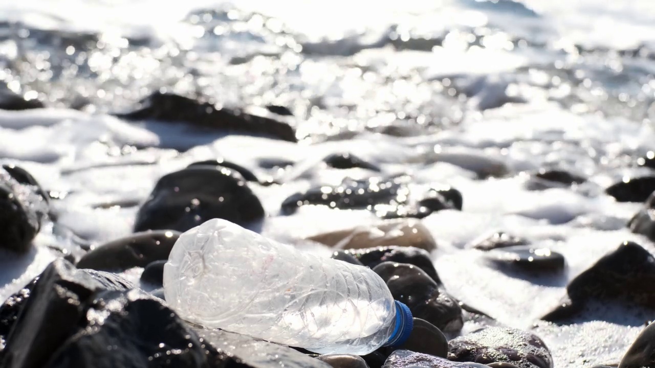 蓝色瓶盖的透明空塑料瓶躺在海边或石滩上的海滨。环境污染，环保人士都敲响了警钟，有必要收集垃圾和塑料垃圾。视频素材