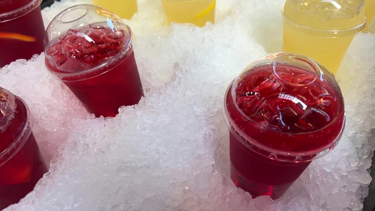 黄色和红色的饮料装在塑料杯里放在冰里樱桃或覆盆子饮料和柠檬慕斯方便的人工雪防止饮料变冷视频下载