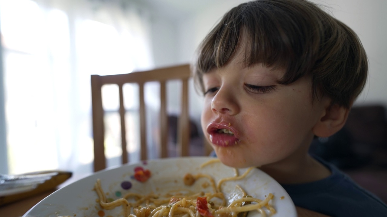 母亲在午餐时间给儿子喂意大利面。父母在家吃饭时用叉子喂孩子吃面条视频素材