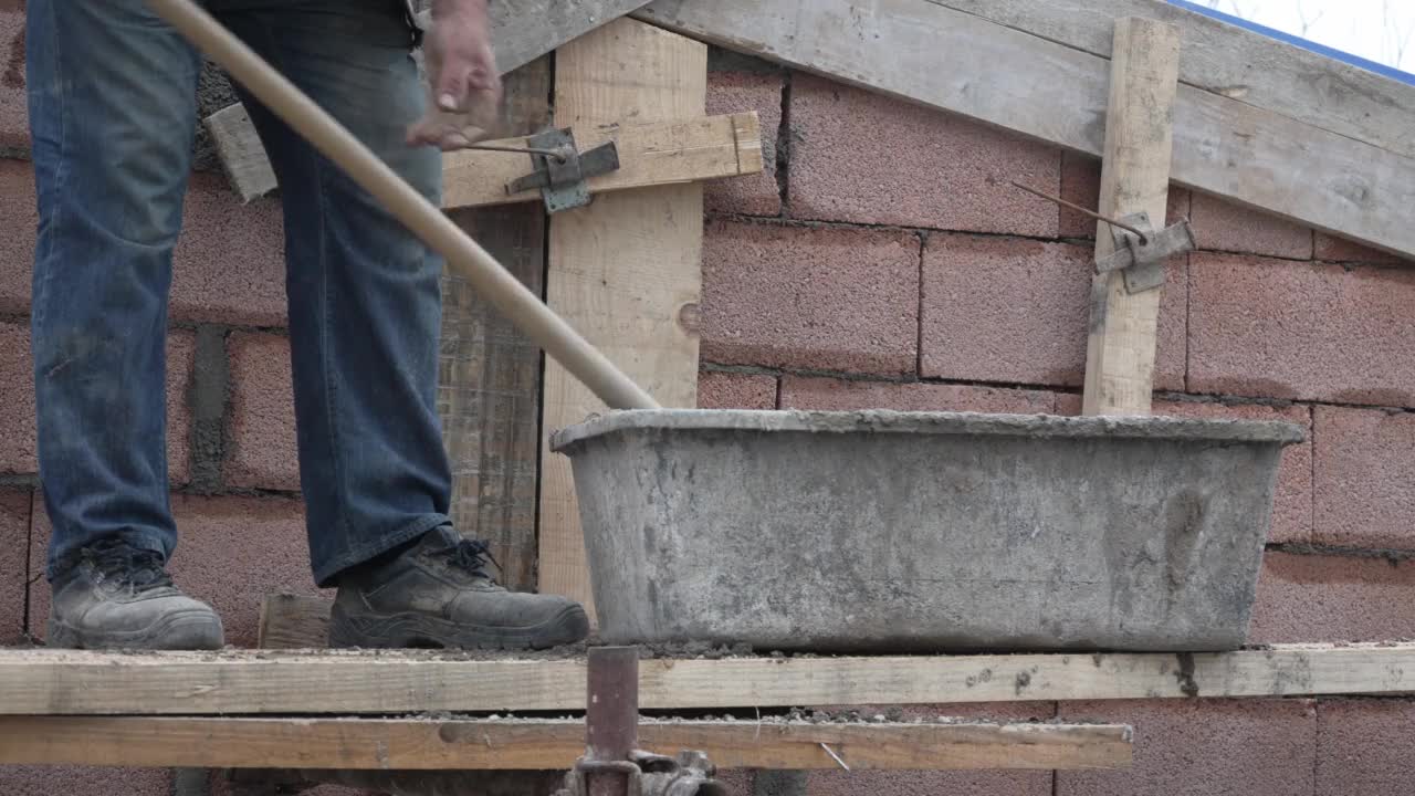工地中段无名男子手持铁锹将水泥混凝土浇筑在建筑墙面上视频素材