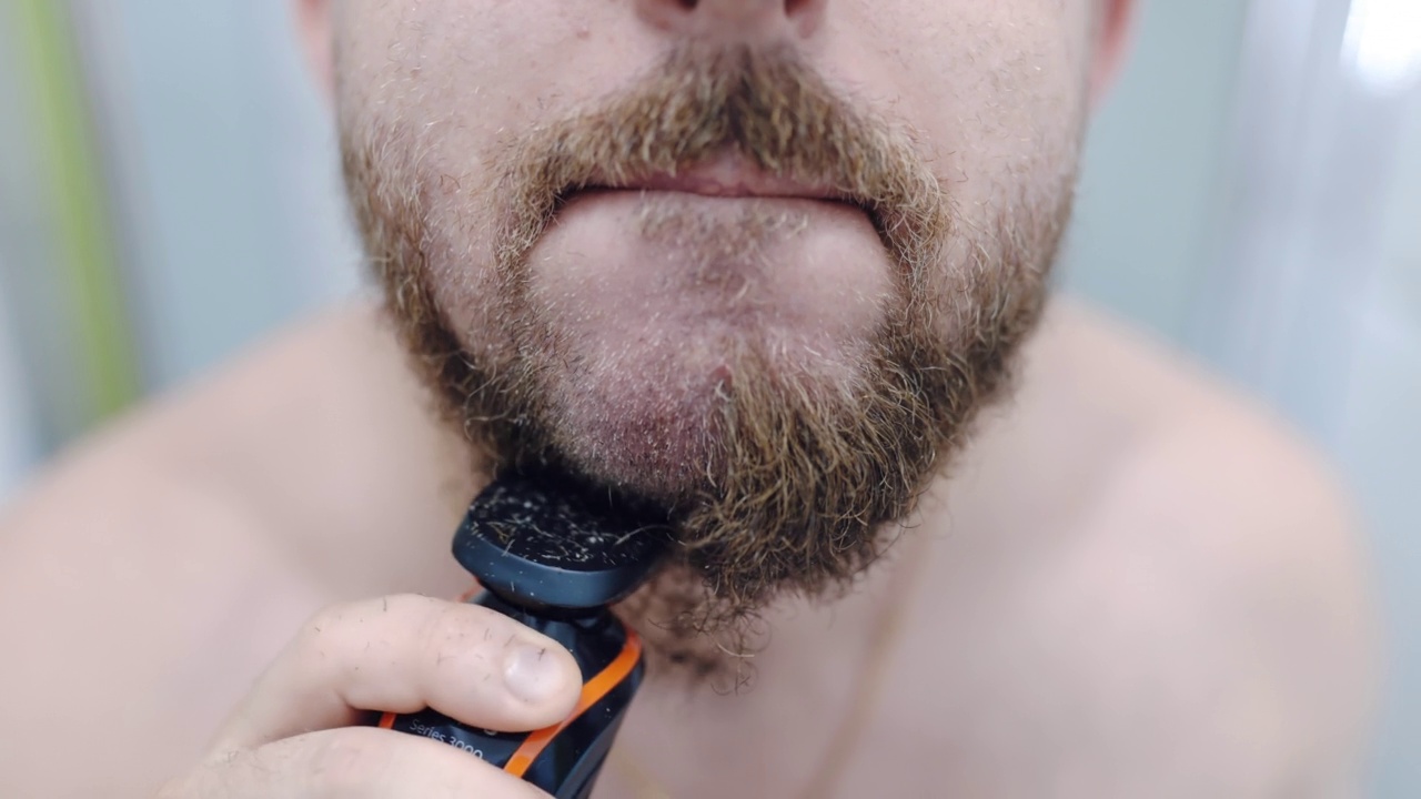 剃须后皮肤干燥或过敏的普遍问题，男性用电动修剪器去除面部毛发，每天在浴室进行面部护理。帅气潮男不刮胡子，刺激性皮肤的面部卫生，男士的美容视频素材