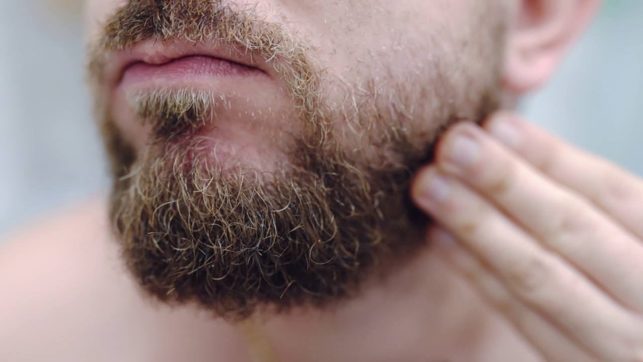 时髦的梳理胡子的工具，男人在浴室做皮肤护理程序。男士早上刮胡子后摸他的厚胡子和梳理，面部皮肤敏感和过敏的问题，卫生和仪容整洁的观念视频素材