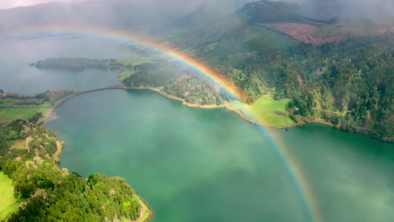 鸟瞰清澈闪亮的水，雾蒙蒙的绿色山脉和彩虹在亚速尔，葡萄牙视频下载