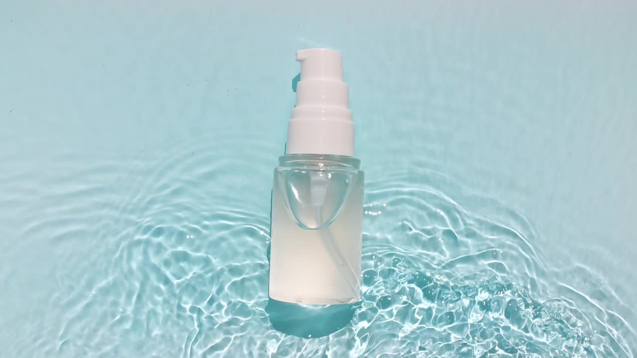 化妆品瓶，小瓶在水面上滴药水。纯净水反射阳光和阴影。缓慢运动的波浪水。包装设计的视频，化妆品的广告视频下载