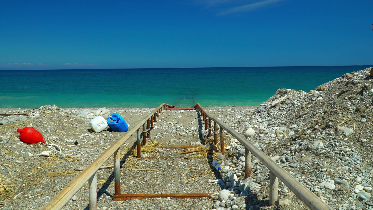 地中海的沙滩和卵石海岸。下水用的栏杆。蓝色无云的天空和天际线为背景。视频下载