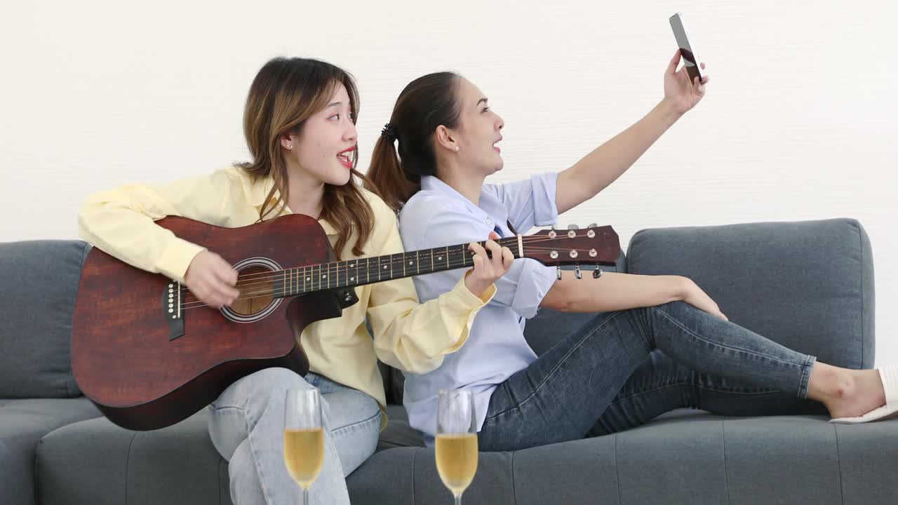 两个女性朋友在家里玩得很开心，弹吉他，唱歌，喝香槟。视频素材