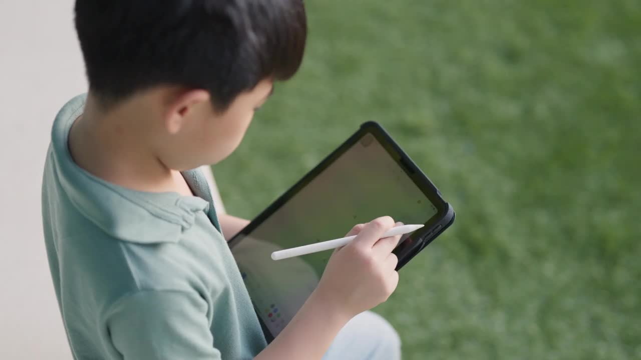 可爱的亚洲男孩坐在公共花园在圣诞节期间使用平板电脑和玩在线游戏的朋友。微笑着享受假期的自由时光。数字餐桌和wifi技术。新一代的新常态生活方式。视频素材