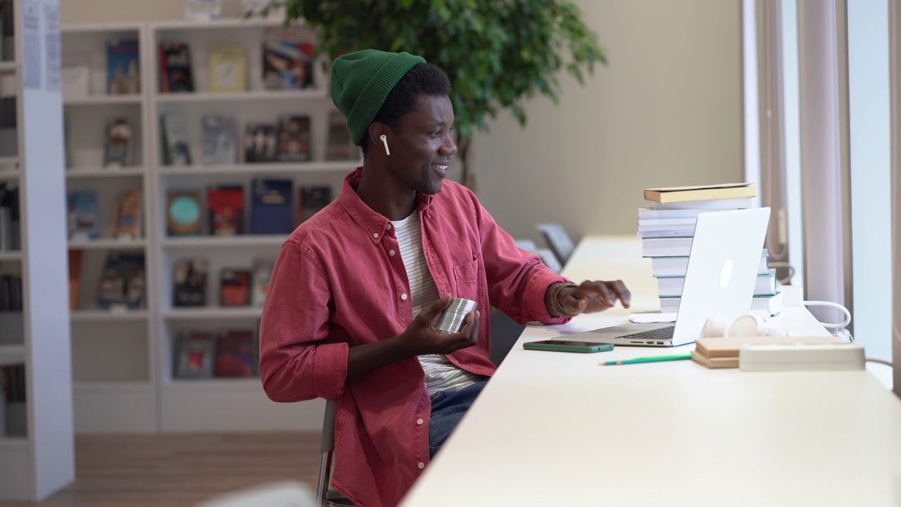 开朗懒惰的非裔美国人，学生，笑着和拖延坐在图书馆的笔记本电脑视频下载