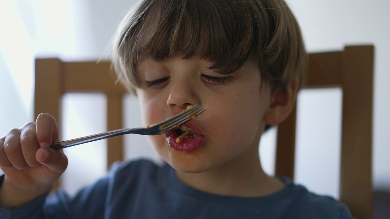 特写孩子的脸吃意大利面。一个金发小孩吃面条意大利面视频素材