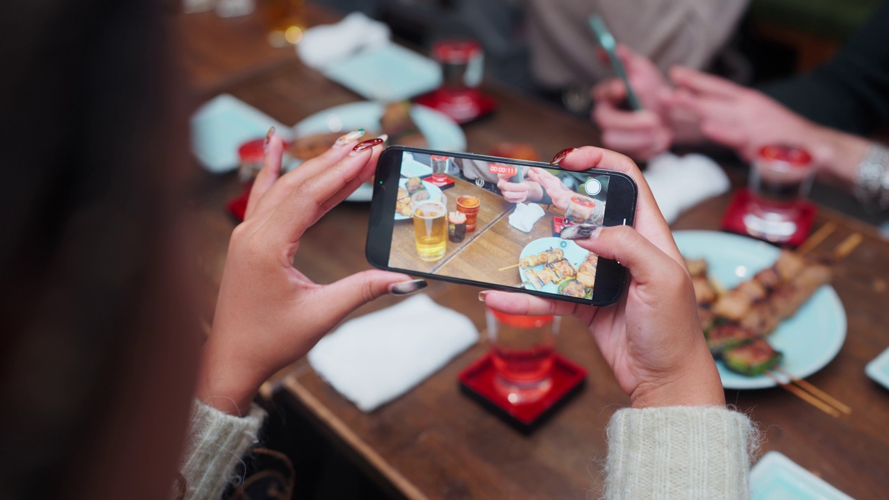 一名女游客享受日式居酒屋，用智能手机拍摄食物和饮料的特写视频视频下载
