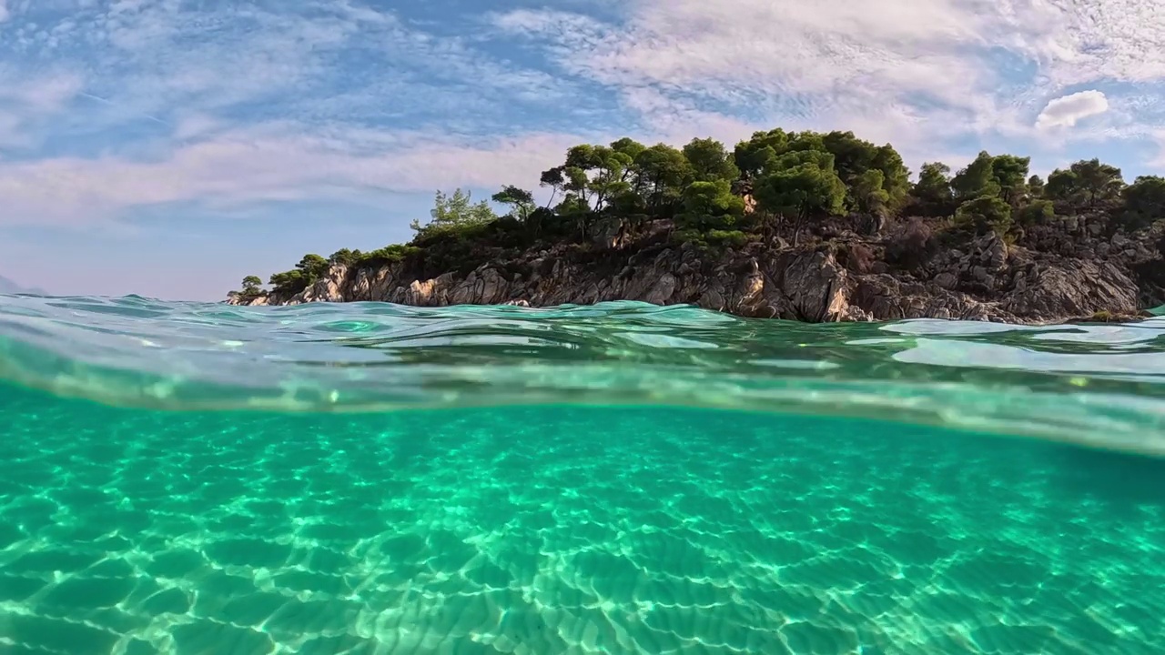 半水下慢动作的沙滩底部和岩石与树木。在希腊哈尔基迪基的西托尼亚，清澈的海水。从空气和水的边界与圆顶射击视频素材