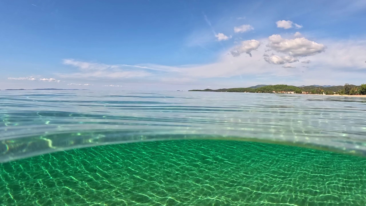 在希腊哈尔基迪基的西托尼亚，清澈的海水。半水下慢动作的沙滩底部，蓝天和云。从空气和水的边界与圆顶射击视频素材