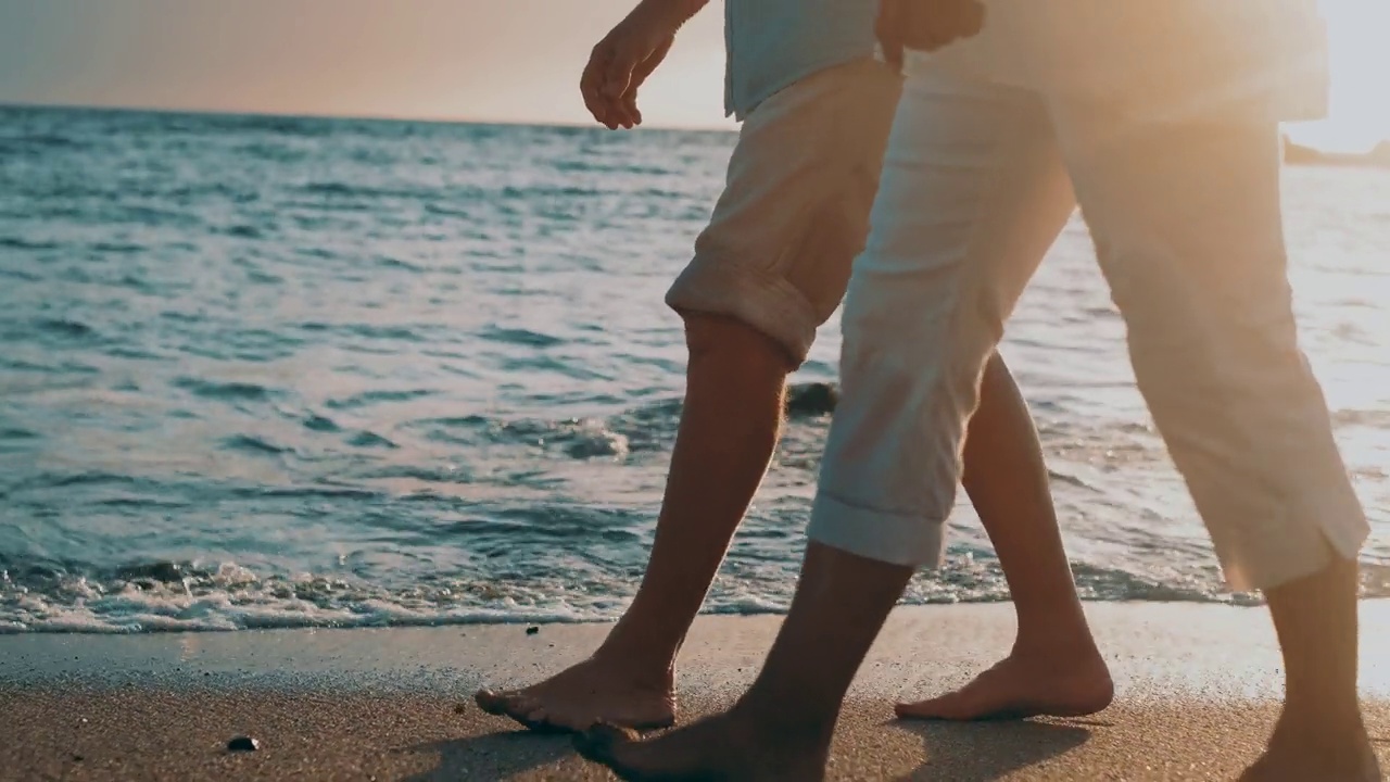 一对成熟的老人一起走在沙滩上，在沙滩上玩得很开心，享受和生活的时刻。两个可爱的高年级学生在一起玩。赤脚走在水面上视频素材