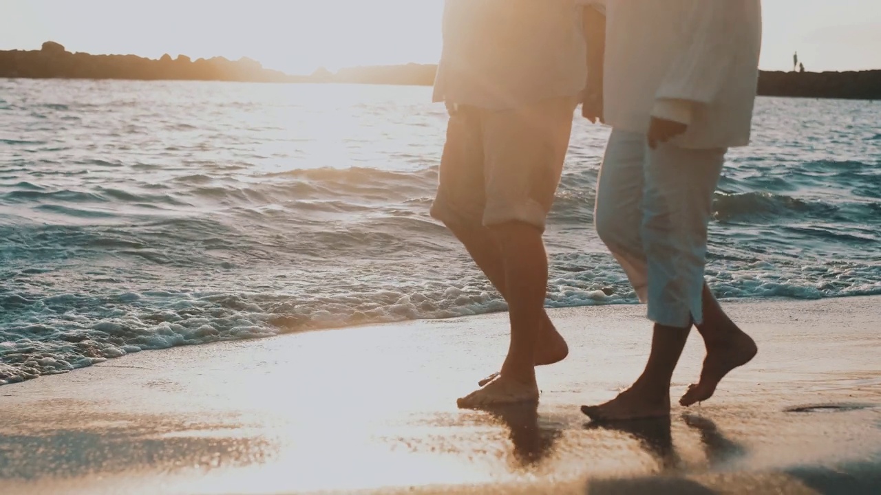 一对成熟的老人一起走在沙滩上，在沙滩上玩得很开心，享受和生活的时刻。两个可爱的高年级学生在一起玩。赤脚走在水面上视频下载