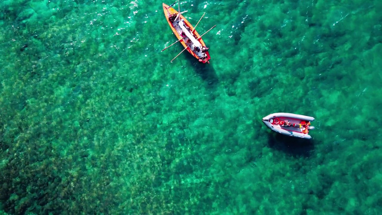 一艘划艇和一艘摩托艇漂浮在蓝绿色的水面上。视频下载