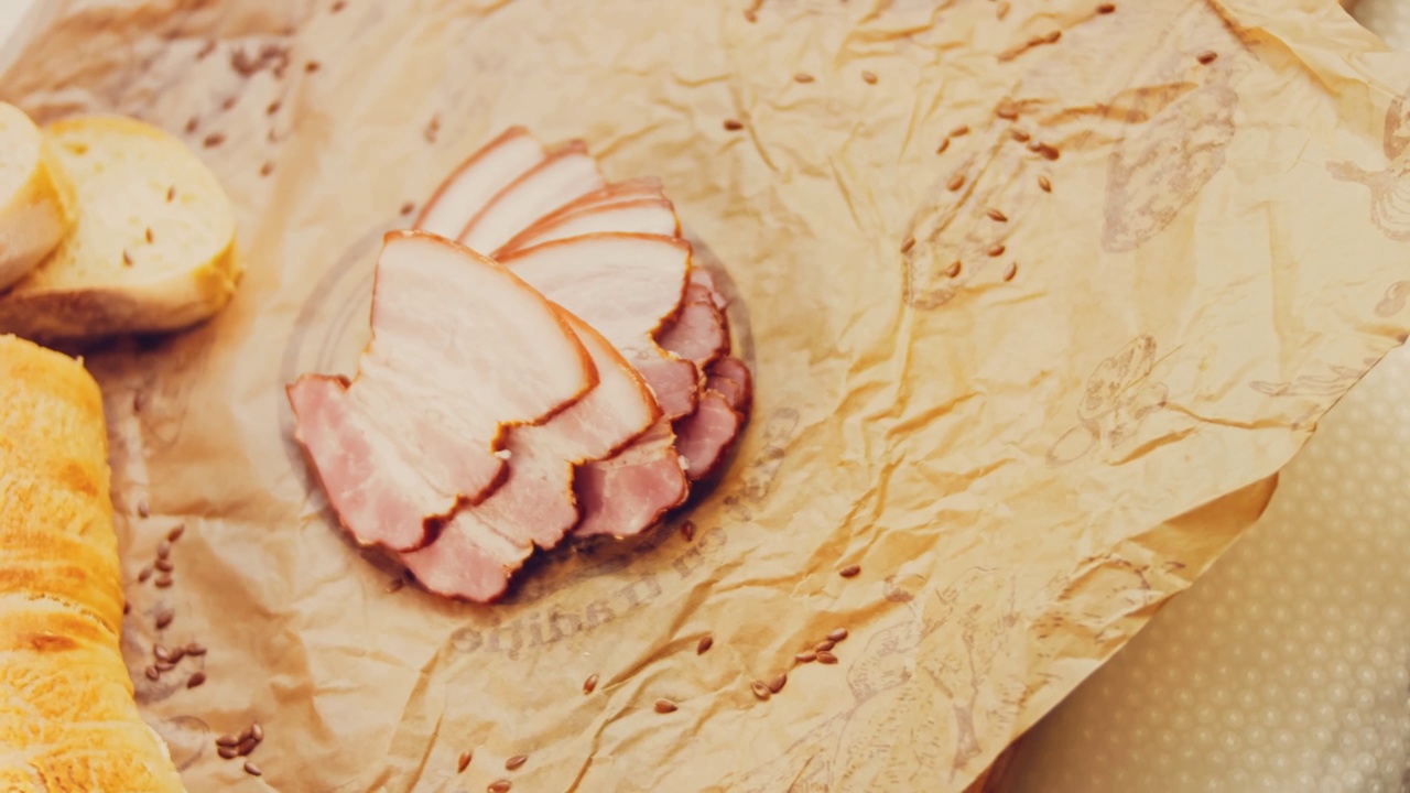 猪肉熏牛肉片与法国法棍的波浪效果。香肠放在复古风格的烹饪托盘上，放在食物纸上。在滑块上进行慢动作拍摄。我们也用新鲜的生菜叶视频下载