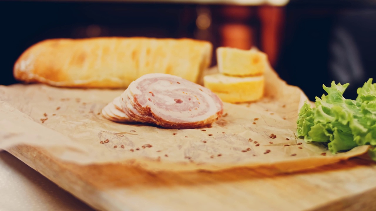 波状效果的猪肉香肠卷切片与法国法棍。香肠放在复古风格的烹饪托盘上，放在食物纸上。在滑块上进行慢动作拍摄。我们也用新鲜的生菜叶视频下载