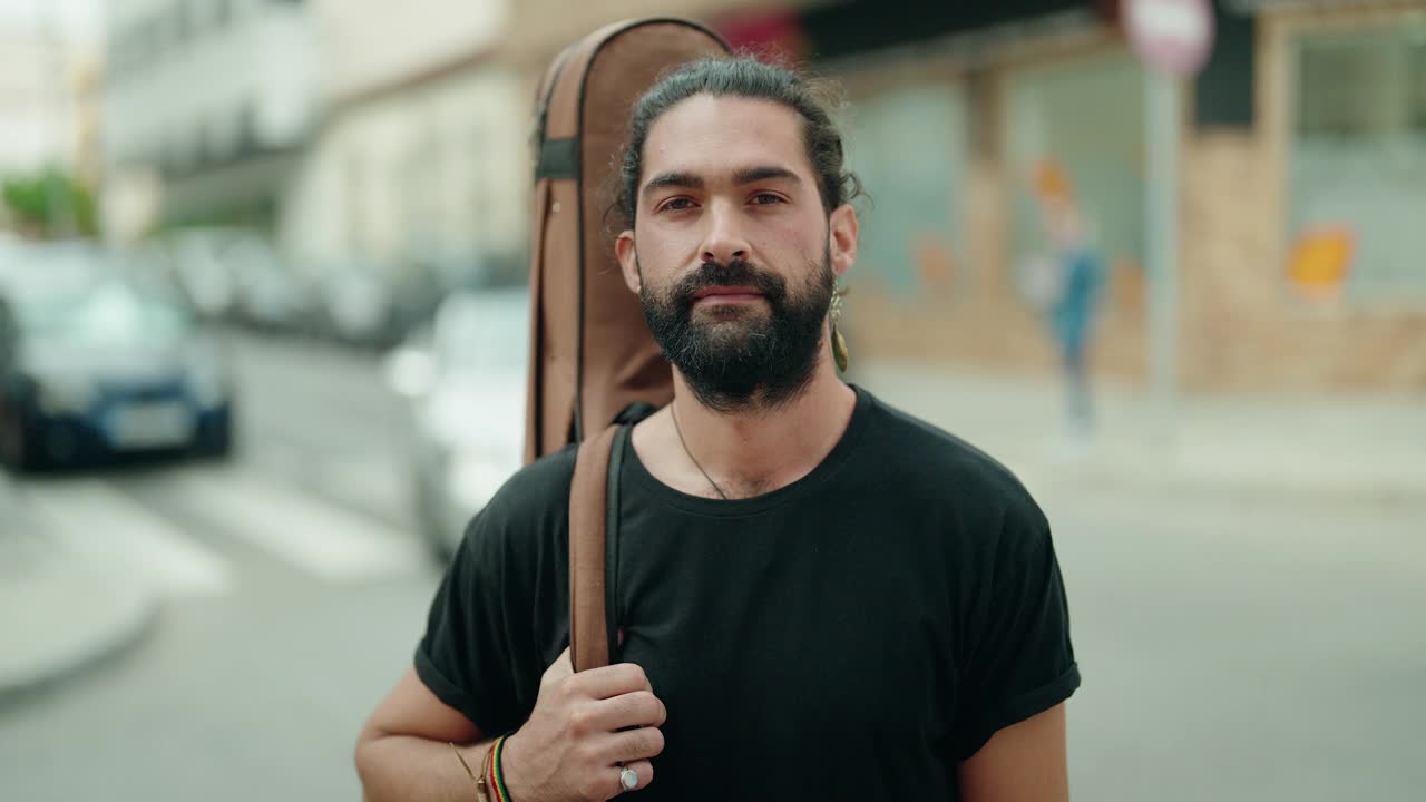 年轻的西班牙男子音乐家微笑自信地抱着吉他案在街上视频素材