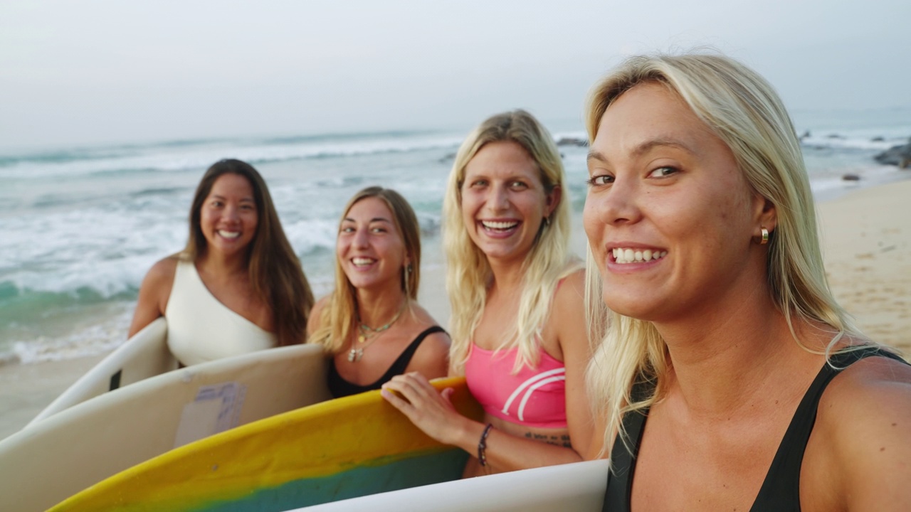 快乐的多种族冲浪女孩在比基尼做视频通话拿着冲浪板面对海滩的相机。性感美丽的年轻冲浪妇女在泳装自拍后会议。朋友videochatting视频下载