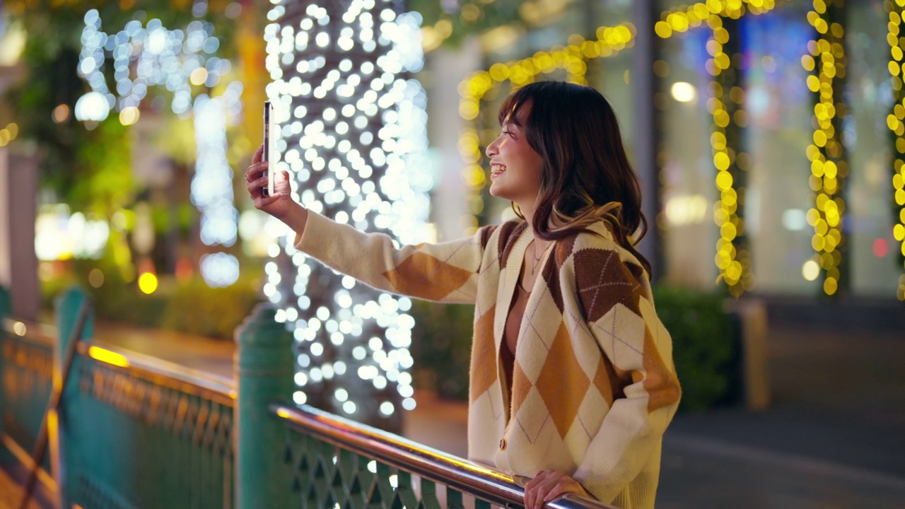 4K年轻的亚洲女子晚上在城市里用手机自拍。视频下载