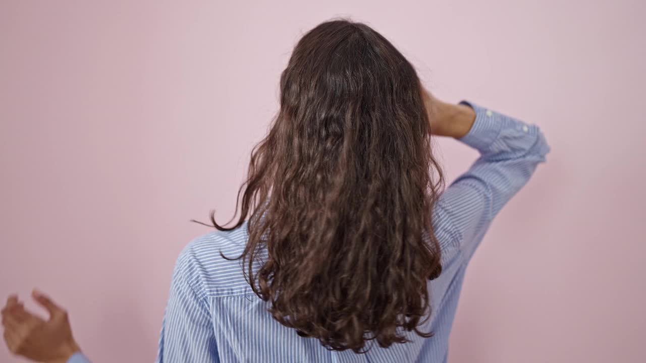 年轻美丽的西班牙女人触摸她的头发向后在孤立的粉红色背景视频素材
