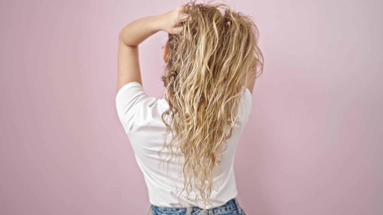 年轻的金发女子在孤立的粉红色背景上向后抚摸她的头发视频素材