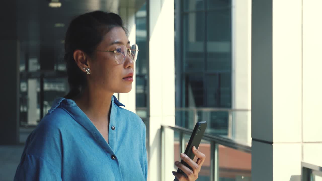 年轻的女商人在一栋漂亮的大楼外用可视电话和同事聊天。视频下载