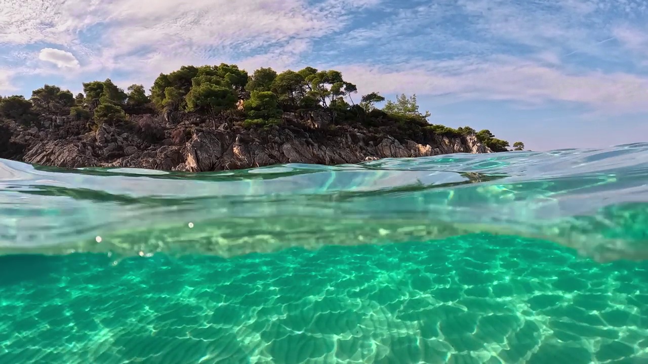 希腊哈尔基迪基岛锡托尼亚清澈的海水。从空气和水的边界与圆顶拍摄。半水下的沙滩底部和岩石与树木的慢动作视图视频素材