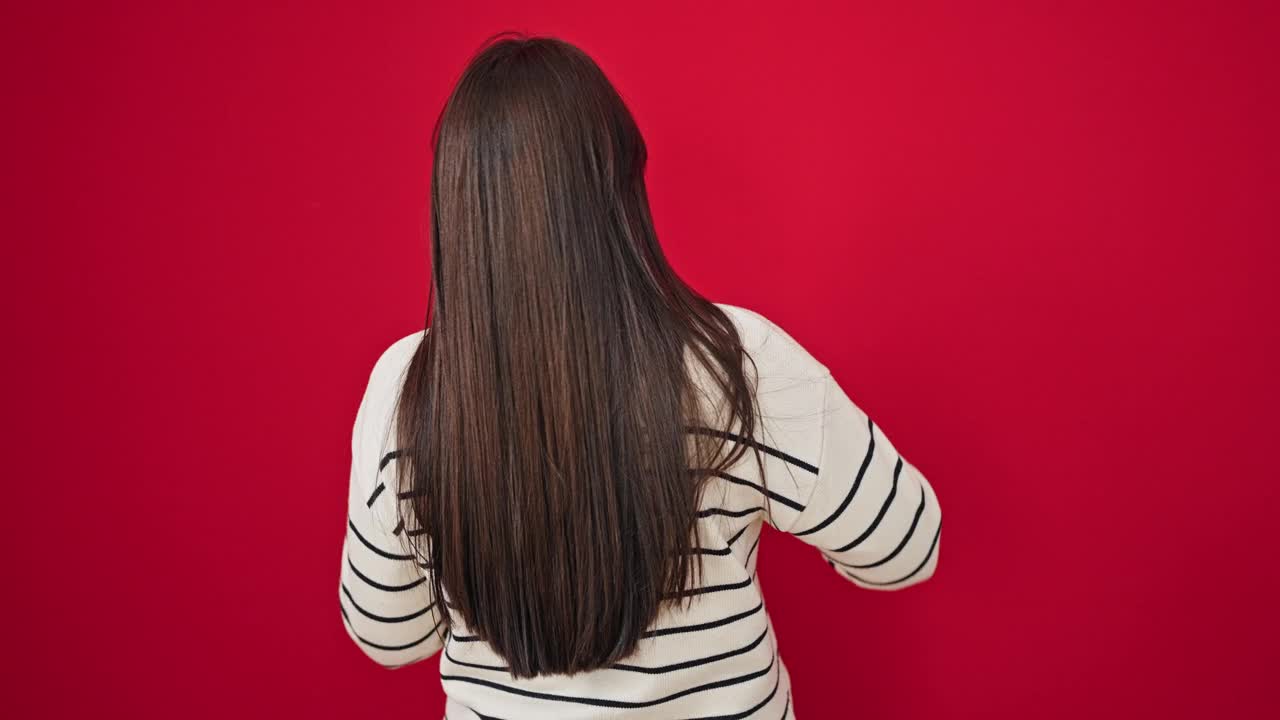 年轻美丽的西班牙女人触摸她的头发向后在孤立的红色背景视频素材