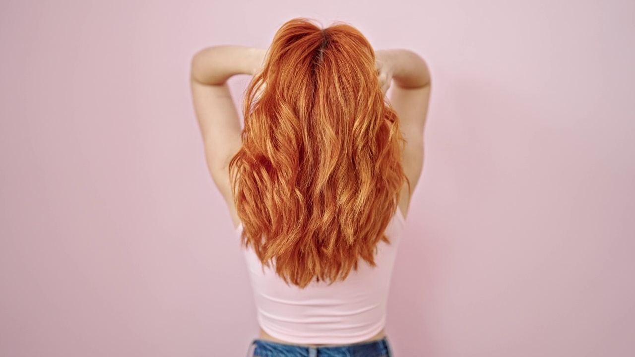年轻的红发女子在孤立的粉红色背景上向后抚摸她的头发视频素材