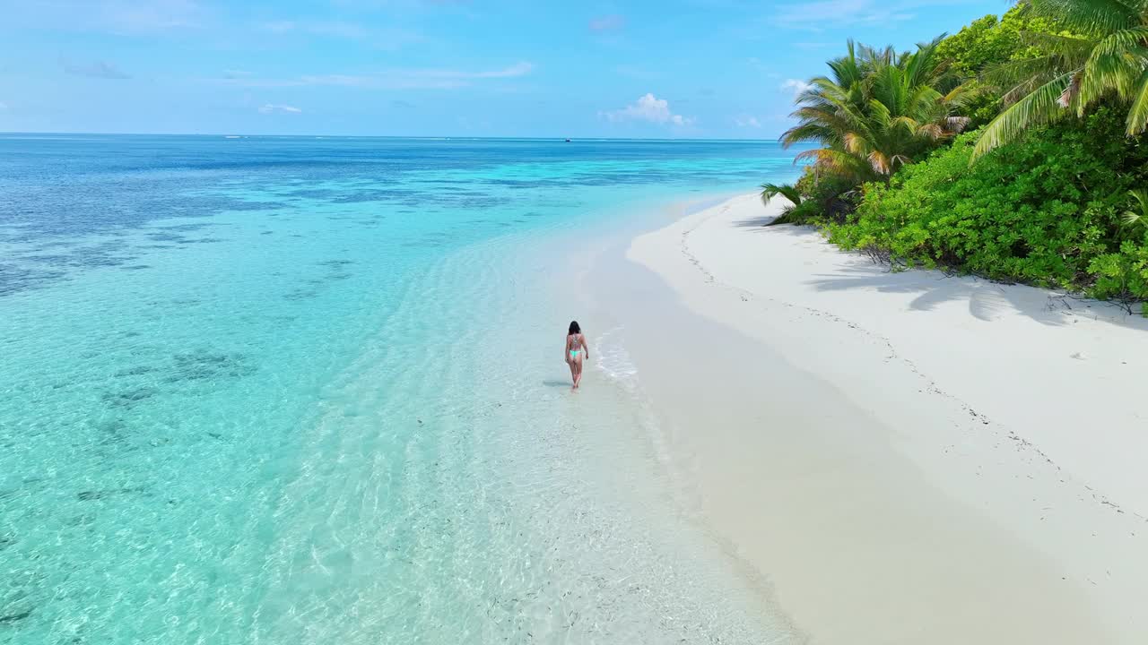 无人机拍摄的年轻女子漫步在热带岛屿的海滩上视频素材