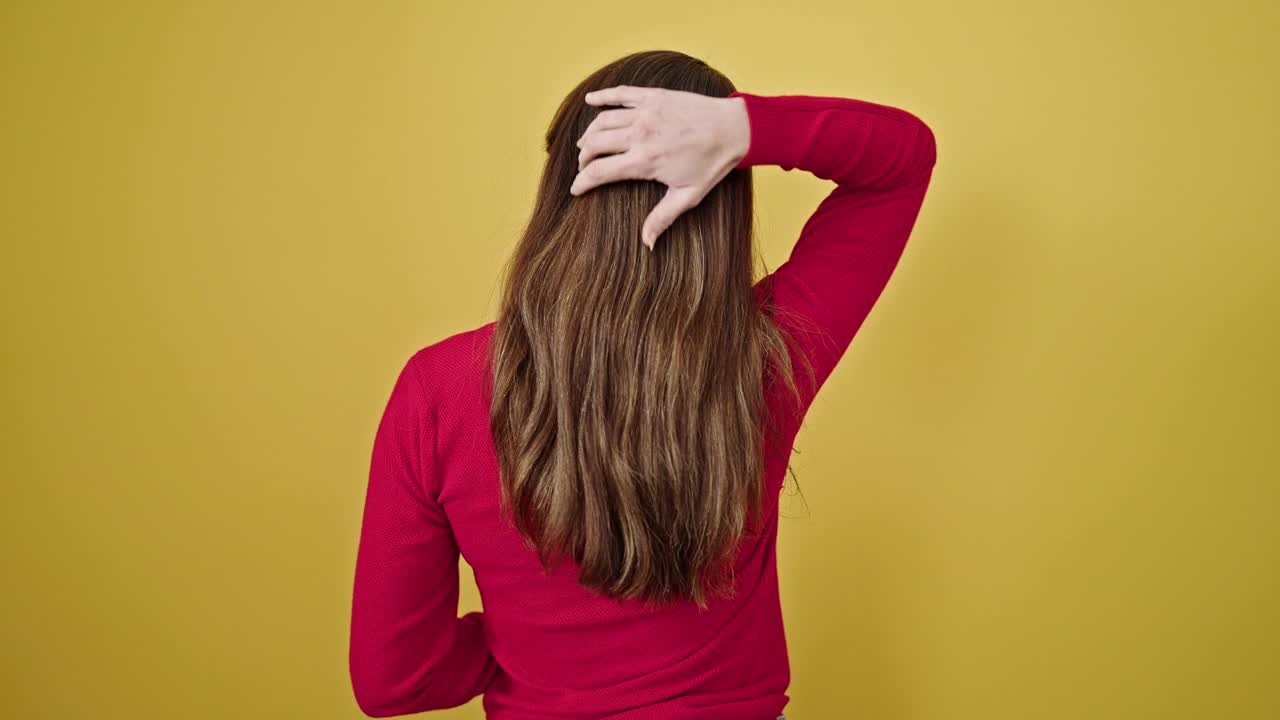 年轻的西班牙女子在孤立的黄色背景上向后抚摸她的头发视频素材